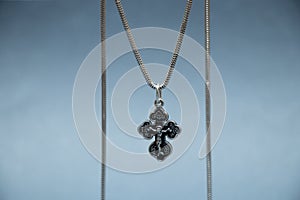 Silver cross and chain hanging on dark blue isolated background close -up