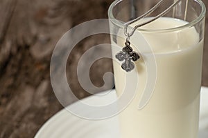 Silver cross and a glass full of milk on a wooden table in the kitchen