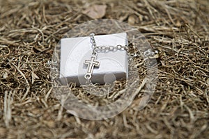 A silver cross necklace sitting in some hay
