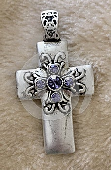 Silver Cross Pendant with Purple Rhinestones Close Up on Textured Background