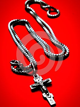 Silver cross on a silver chain in the form of the letter & x22;N& x22; on a red background
