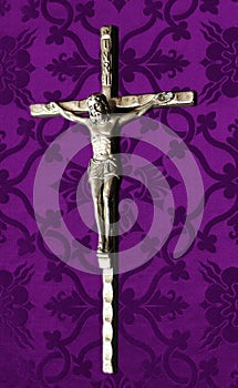 Silver crucifix placed on purple cloth. Lenten concept