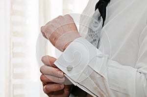 Silver cufflink that a man is putting on the cuff of his white shirt.