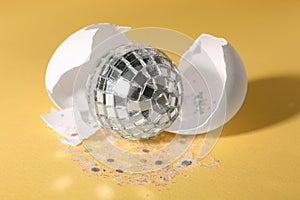 Silver disco ball, broken eggshell and glitter sprinkles on yellow background, closeup