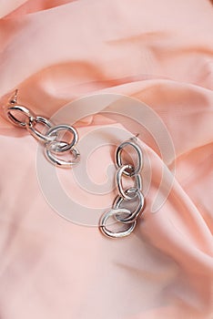 Silver earrings on an expensive pale pink silk background. Beautiful female jewelry. Chain earrings