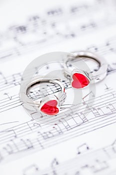 Silver earrings with red hearts on blurred music notes background