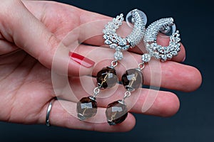 Silver earrings with rhinestones in hand on a dark background