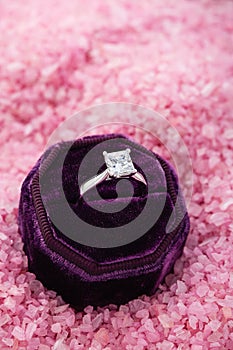 Silver engagement ring with big diamond in purple gift box on pink background