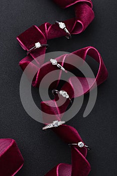 Silver engagement rings with diamonds on black background with burgundy red ribbon