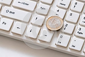 Silver euro coin with a gilded border close-up lies on the key with the number one. White computer keyboard. Shareholders on the