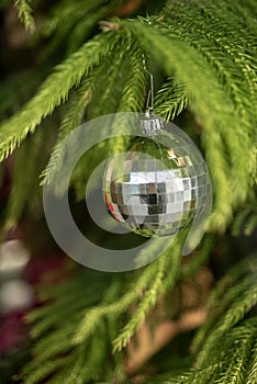 Silver faceted ball ornament hanging from branch of green fir tree Christmas decoration