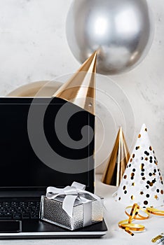 Silver festive box and blank screen laptop with party hats and balloons.