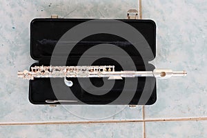 The silver flute is in a black box placed on the floor.