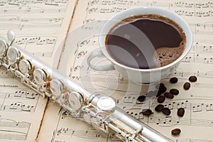 Silver flute, cup of coffee and coffee beans on an ancient music score