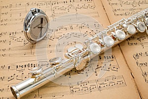 Silver flute and pocket metronome on an ancient music score