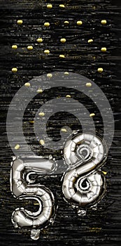 Silver foil balloon number 58 on a background of black tinsel with gold confetti. Birthday card, inscription fifty