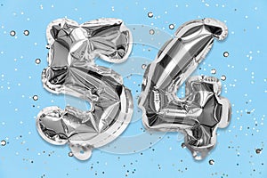 Silver foil balloon number, digit fifty four on a blue background with sequins. Birthday card with inscription 54