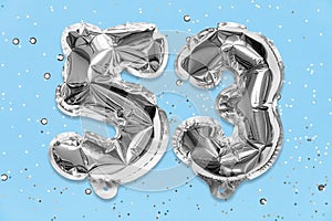 Silver foil balloon number, digit fifty three on a blue background with sequins. Birthday card with inscription 53