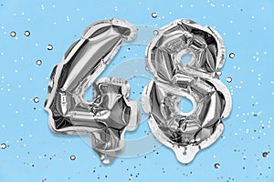 Silver foil balloon number, digit forty eight on a blue background with sequins. Birthday card with inscription 48