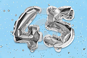 Silver foil balloon number, digit forty five on a blue background with sequins. Birthday card with inscription 45