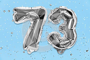 Silver foil balloon number, digit seventy three on a blue background with sequins. Birthday card with inscription 73