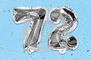 Silver foil balloon number, digit seventy two on a blue background with sequins. Birthday card with inscription 72