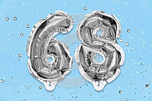 Silver foil balloon number, digit sixty eight on a blue background with sequins. Birthday card with inscription 68