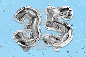 Silver foil balloon number, digit thirty five on a blue background with sequins. Birthday card with inscription 35