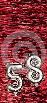 Silver foil balloon number number 58 on a background of red tinsel decoration. Birthday greeting card, inscription fifty
