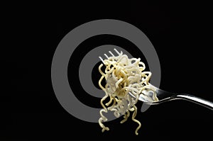 Silver fork and just cooked noodles on it against dark background.Empty space