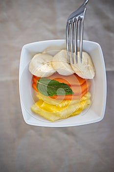 Silver fork pocking sliced fruit on square white plate