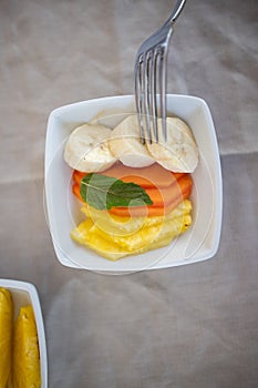 Silver fork pocking sliced fruit on square white plate