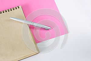 A silver fountain pen and an eco-friendly notepad made from recycled materials lie on a pink and white surface. Copy space