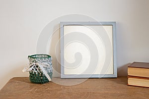 Silver frame mock up ,on old table and white wall , with books and crocheted pot