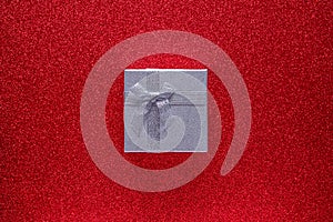 Silver gift box on glitter red background with copy space. Top view. Flat lay