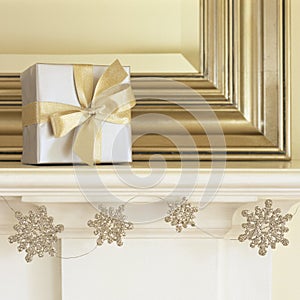 Silver and gold Christmas gift present on mantel with glitter snowflake garland. Beautiful, elegant, fancy holiday home interior photo