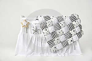 Silver and gold star shaped pillows and patchwork comforter on a white baby cot