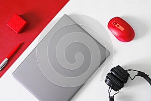 Silver gray laptop or ultrabook, fountain pen, red computer mouse, red box and black headphones on a red and white background. The