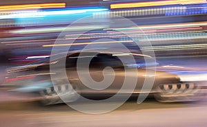 A silver grey car seen in a motion blur at night with a light streaks background