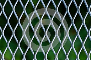 Silver grid of metal fence with blurred green color background