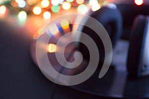 Silver headphones lying on vintage black vinyl long play record with colorful disco lights in the background. Abstract blurred