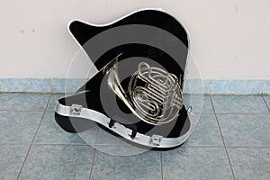 The silver horn instrument housed in a black box placed on the floor.