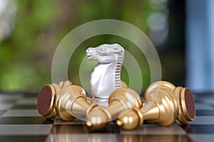 A silver horse piece surrounded by a pile of golden pawn pieces on a chess board