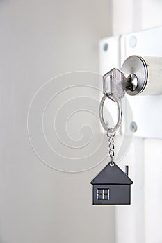 Silver house key in white door, with little keychain house, opening door to new house, home, investment, real estate concept,