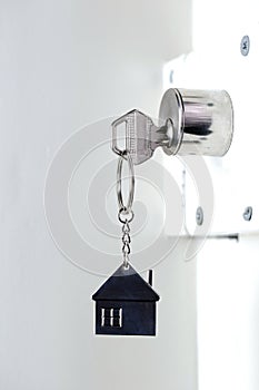 Silver house key in white door, with little keychain house, opening door to new house, home, investment, real estate concept,