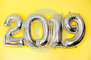 Silver inflatable balloons in the shape of numbers 2019 on the yellow background