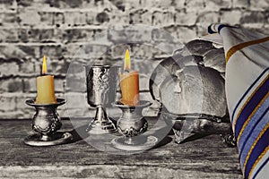 Silver kiddush cup, crystal candlesticks with lit candles, and challah