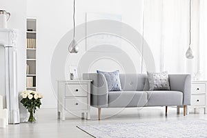 Silver lamps above white cabinets in apartment interior with flowers and grey settee. Real photo