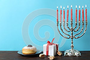 Silver menorah near dreidels with He, Pe, Nun, Gimel letters, gift box and sufganiyah on wooden table, space for text. Hanukkah