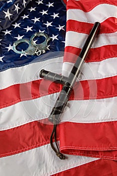 Silver metal handcuffs and police nightstick over US flag on flat surface
